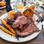 Roast beef on a white plate with roast potatoes and Yorkshire pudding with vegetables