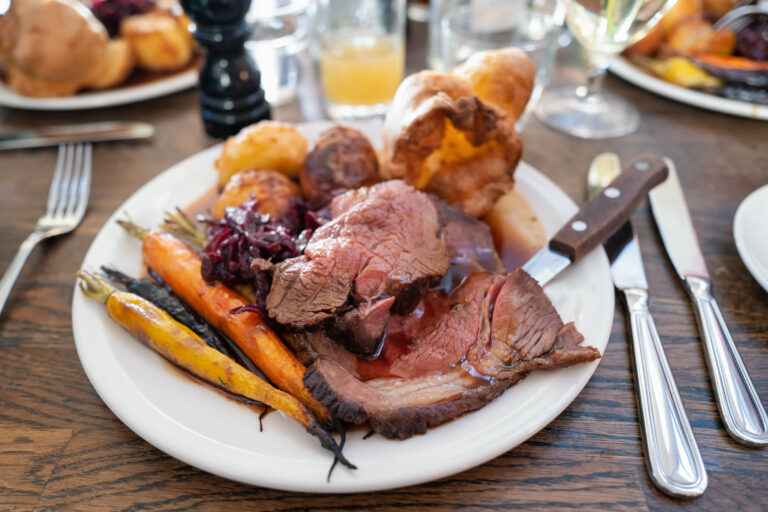 Roast beef on a white plate with roast potatoes and Yorkshire pudding with vegetables